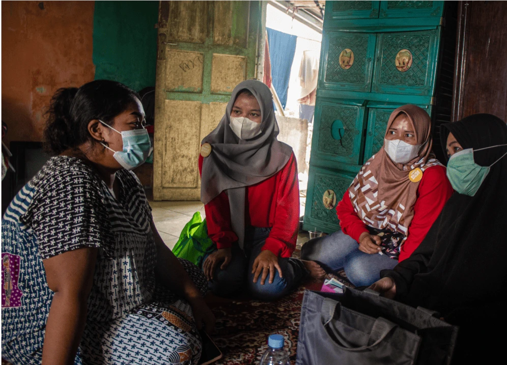 Tiga orang kader kesehatan sedang melakukan kunjungan rumah dan berkomunikasi dengan seorang perempuan yang merupakan warga setempat. Pada foto ini kader sedang mendengarkan keterangan darinya.